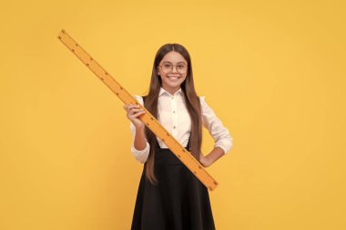 Okul üniformalı ve gözlüklü neşeli çocuk ölçüm ve geometri için matematik cetveli tutuyor.