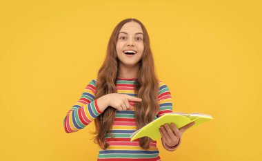 Mutlu çocuk gülümsüyor okul kitabı sarı arka planını işaret ediyor, çalışıyor..