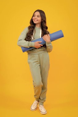 12, 13, 14 yaşlarında spor takım elbiseli bir kız. Spor kıyafetleri içinde moda bir çocuk. Sportif modaya uygun kıyafet. Sarı arkaplanda stüdyo çekimi