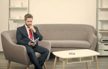 Takım elbiseli olgun bir işadamı planlamacıyla ofiste oturur..