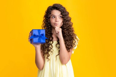 Child with gift present box on isolated studio background. Gifting for kids birthday. Thinking face, thoughtful emotions of teenager girl