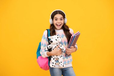 Heyecanlı bir yüz. Sarı arka planda izole edilmiş oyuncağı olan komik okul kızı. Mutlu bir çocukluk ve çocuk eğitimi. Şaşırtıcı bir ifade, neşeli ve mutlu.