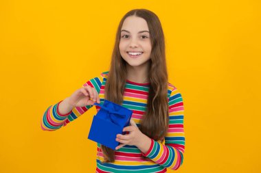 Sarı arka planda izole edilmiş hediye kutusunu tutan genç kız çocuğu. Çocukların doğum günü hediyesi.