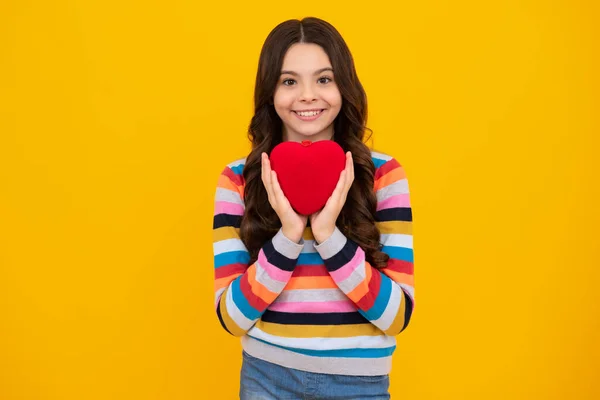 Cheerful lovely romantic teen girl hold red heart symbol of love for valentines day isolated on yellow background. Happy teenager, positive and smiling emotions of teen girl