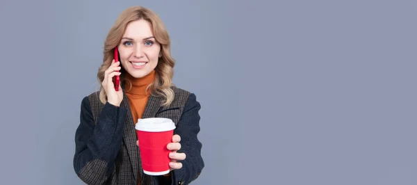 Happy woman talk on mobile phone giving hot cup grey background, tea. Woman portrait, isolated header banner with copy space