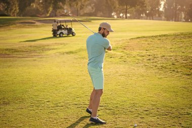Golf sopasıyla şapkalı golfçünün tam boy portresi. İnsanların yaşam tarzı. Adam yeşil çimlerde oyun oynuyor. Yaz etkinliği. Profesyonel açık hava sporu. Profesyonel golf sahasında erkek golfçü.
