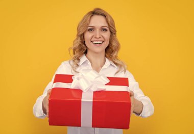 Sarı arka planda büyük hediye kutusuyla gülümseyen kadın..