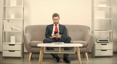 Ofiste oturan işadamı ve telefondaki e-postayı kontrol ediyor.