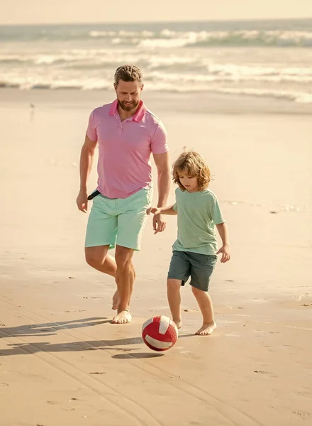smiling father and son play football on summer beach with ball, fathers day.