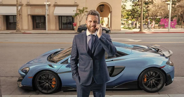 handsome businessman talk on phone next to luxury car.