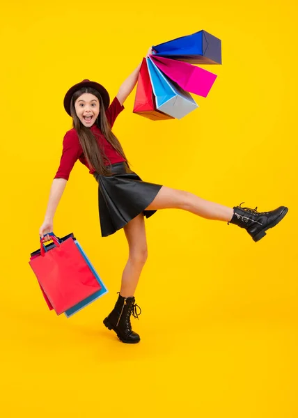 Funny teen girl hold shopping bag enjoying sale isolated on yellow. Portrait of teenager schoolgirl is ready to go shopping. Run and jump. Excited teenager, glad amazed and overjoyed emotions