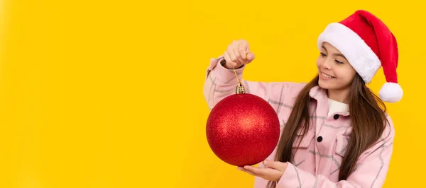 黄色の背景に赤い装飾ボールを持つ10代の女の子 クリスマスの飾りだ クリスマスの子供の女の子のバナー スタジオの子供の冬の肖像画とともにコピースペース — ストック写真
