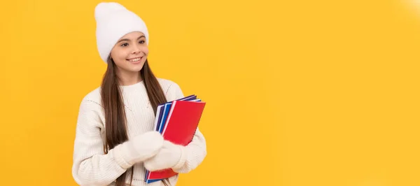 冬の学校 冬の帽子と手袋の子供は黄色の背景 コピースペース 学校でワークブックを保持します 女子学生の肖像画 スタジオバナーヘッダー 学校の子供の顔 コピースペース — ストック写真