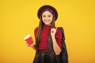 12, 13, 14 yaşlarındaki çocuk elinde bir fincan kapuçino ya da çay ile. Sarı arka planda yemek kupası olan ergen, sabah içeceği. Mutlu ergen portresi. Gülümseyen kız