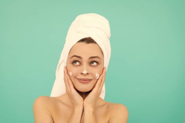 Neşeli genç kız mavi arka plana yüz kremi sürüyor..