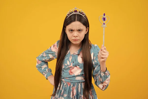 Angry teenager girl, upset and unhappy negative emotion. Portrait of girl princess in tiara holding magic wand. Teenager queen with golden crown