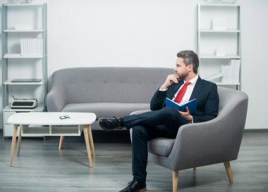 Takım elbiseli olgun bir işadamı ofiste oturup not defterine not alır. karar vermek.