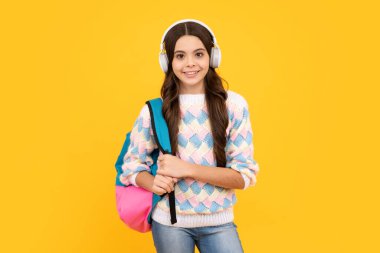 Liseli kız, kulaklıklı genç kız, sarı izole stüdyo geçmişiyle. Okul ve müzik eğitimi kavramı. Okula geri dön.