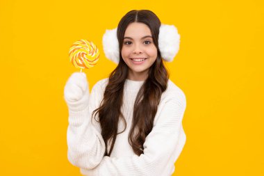 Şekerli lolipop yiyen genç bir kız. Çocuklar için şeker ve şeker. Çocuk, sarı izole arka planda lolipop dondurması yiyor. Lezzetli karamel, şekerci dükkanı. Mutlu gülümseyen kız