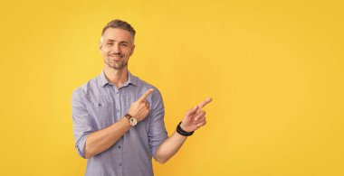 Gülümseyen, bilek saati olan yetişkin bir adam sarı arka planda işaret parmağı, kopyalama alanı, toplantı dakikaları.