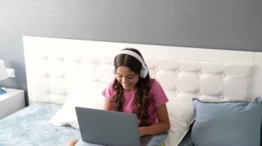 Online eğitim için akıllı telefon ve dizüstü bilgisayar kullanan kulaklıklı mutlu küçük bir kız..