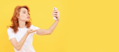 Gadget bağımlısı. Selfie kız blogcu sarı arka plan. Kadın akıllı telefona el öpücüğü veriyor. İzole edilmiş yüz portresi, taklit alanı olan pankart