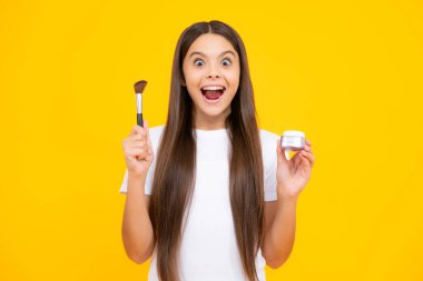 Güzellik, makyaj ve çocukların makyaj malzemeleri. Yüzüne kızaran fırçalı ergen bir kız çocuğu arka planda izole edilmiş. Heyecanlı bir genç, şaşkın ve neşeli duygular içinde