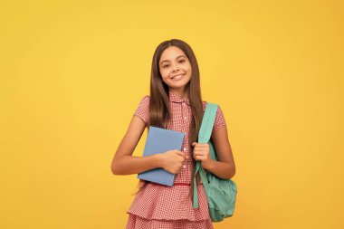 1 Eylül. Mutlu çocukluk. Okul çantalı çocuk. Neşeli genç kız sırt çantası taşıyor. Okula dönüyorum. Bilgi günü. Eğitim konsepti. sarı arka planda çalışma kitabı olan çocuk.