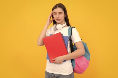 Kulaklık takan yorgun bir kadın sarı arka planda not defteri tutuyor..