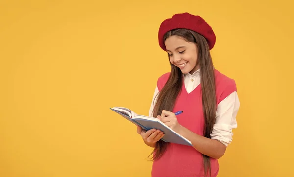 happy teen school girl in french beret making notes in planner notepad or notebook, knowledge.