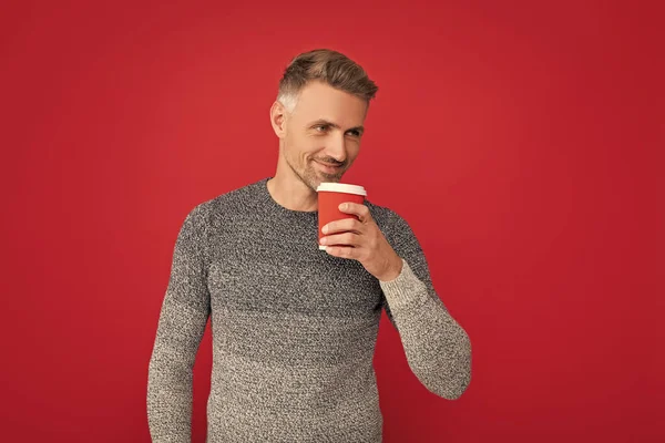 morning coffee. smiling grizzled guy in sweater on red background. hoary man drinking coffee. male fashion model hold cup. winter fashion.