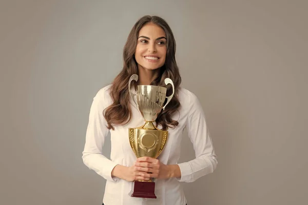Winning businesswoman holding a trophy. Business woman with prize. Business woman with golden cup and fist up gesturing, isolated on gray. Successful employee holds winner cup. Best manager