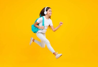 Sırt çantalı liseli kız apoleti öğrenmeye hazır tutuyor. Okul çantalı çocuklar izole edilmiş sarı stüdyo geçmişine sahipler. Heyecanlı genç, atla ve kaç, zıplayan çocuk