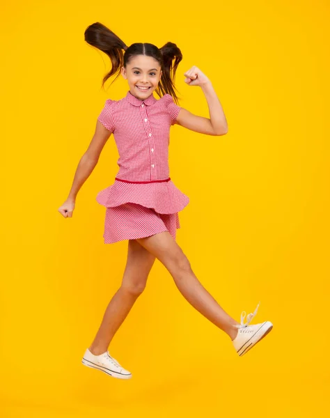 Happy teenager, positive and smiling emotions of teen girl. Full size photo of positive teen girl jump with movement summer dress, fashion kids outfit isolated over yellow background