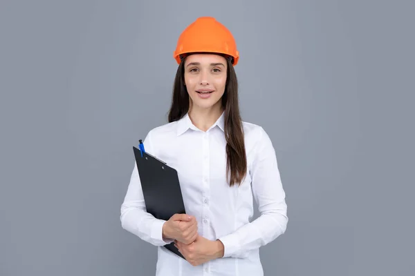 Young woman in hard hat helmet with clipboard isolated on grey background. Architect woman wear helmet and shirt. Business woman, construction manager, builder