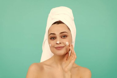 Neşeli genç kadın mavi arka plana yüz kremi sür..