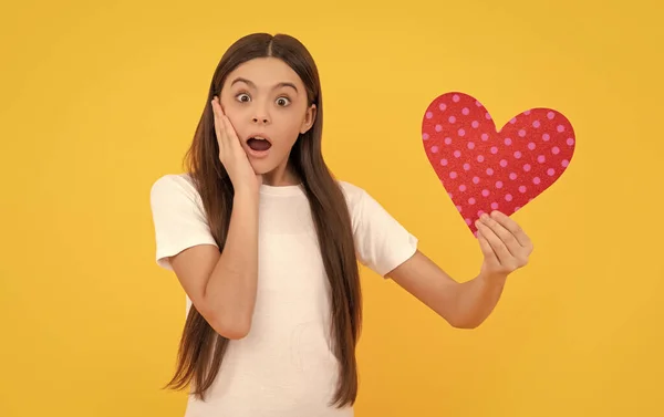 shocked kid with love romantic gift. sweetheart. valentines sale. portrait of child with heart. happy valentines day. be my valentine. teen girl on yellow background. love present.