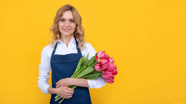 幸せな花売り手女性でエプロンで春チューリップの花で黄色の背景 — ストック写真