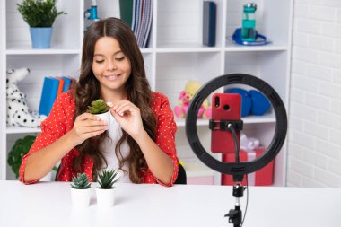 Teen girl blogger influencer use selfie led lamp and smartphone on tripod for making online video tutorial. Teenager vlogger making vlog for kids channel. Happy smiling girl