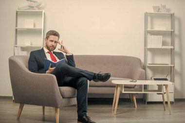 Takım elbiseli olgun bir ofis çalışanı ofiste oturup kitap okuyor..