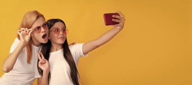 Anne ve kız çocuk afişi, kopyalama alanı, izole edilmiş arka plan. Neşeli anne ve kızı akıllı telefondan selfie çekiyor, aile selfie 'si.