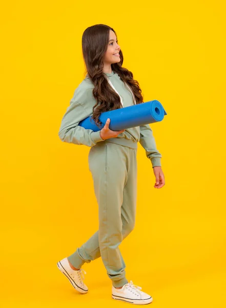 Teen girl dressed in sports uniform. Teenager in a posh stylish sports suit in a hoodie with a hood hold yoga mat. Advertising sportswear tracksuit. Healthy kids lifestyle, sport