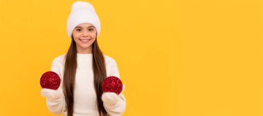 Kış kızı. Kış şapkalı ve eldivenli mutlu çocuk sarı arka planda dekoratif yeni yıl baloları tutuyor, Xmas. Noel çocuğu, stüdyo çocuğu kışın fotokopi çekilen portresi