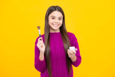 Genç kız makyaj yapıyor, pudra ve fırça tutuyor. Sarı arkaplanda toz fırçası kullanarak makyaj yapan güzel bir genç.