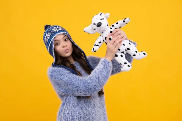 Childhood, toys and kids. Cute teen girl in winter hat cuddling fluffy toy. Funny face