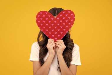 Neşeli romantik genç kız sarı arka planda izole edilmiş sevgililer günü için aşkın kırmızı kalp sembolünü taşıyor.