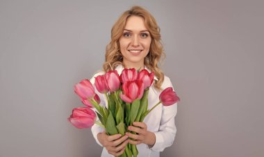 Mutlu genç kadın gri arka planda bahar lale çiçekleri tutuyor..