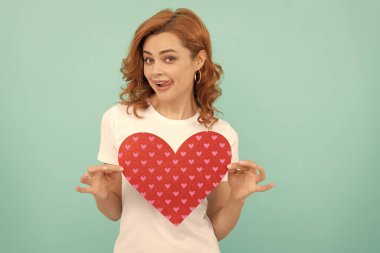 Mutlu kızıl kadın mavi arka planda kırmızı kalbi tut..