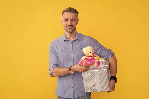 情人节快乐的男人拿着黄色背景的礼盒和玩具 — 图库照片