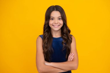 Mutlu kız yüzü, pozitif ve gülümseyen duygular. Genç kız sarı arka planda izole bir şekilde kollarını kavuşturmuş. Kopya alanı oluşturulmuş çocuk portresi